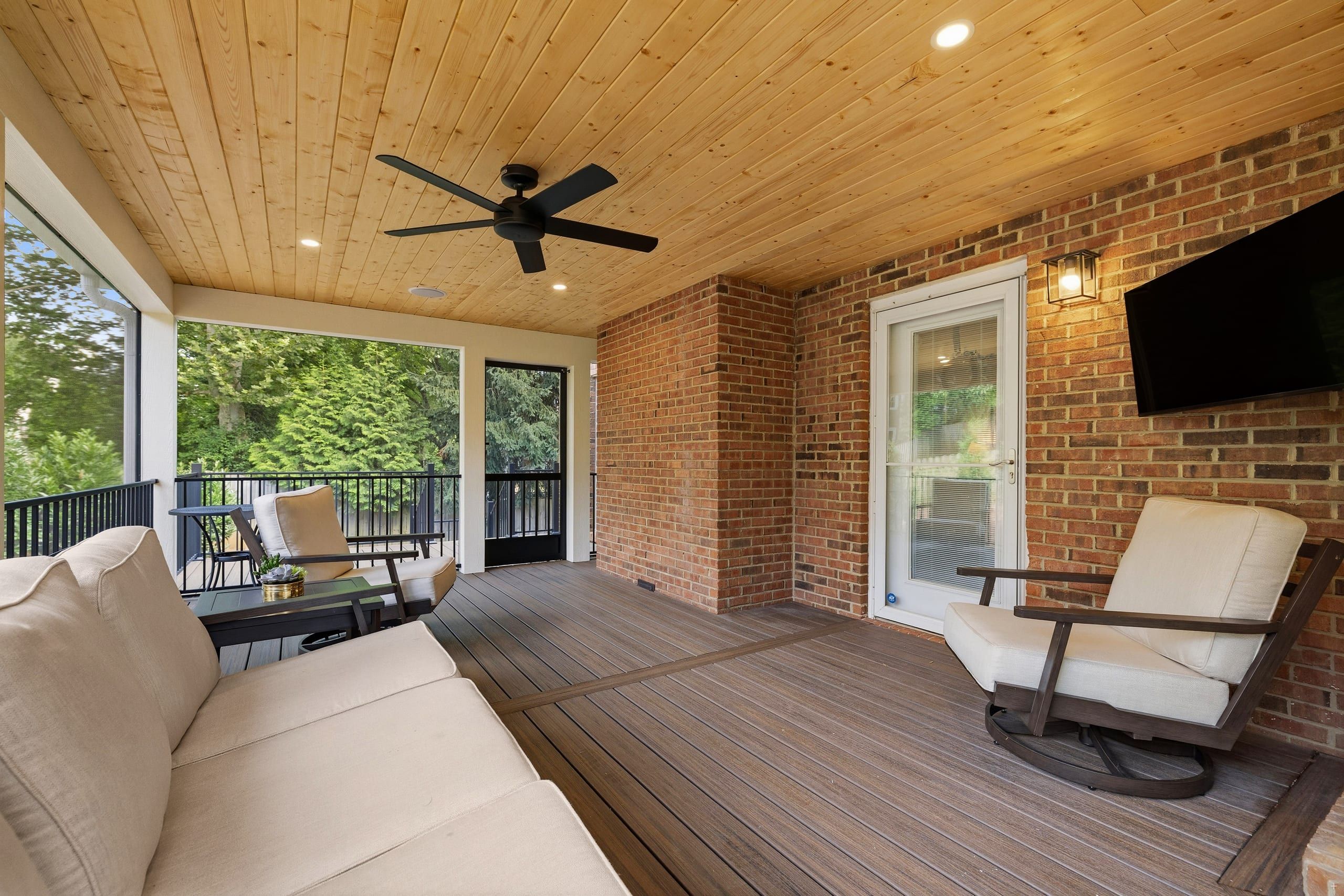 Ashgrove screened porch with a natural tongue-and-groove wood ceiling, black ceiling fan, and Trex Enhance Naturals decking