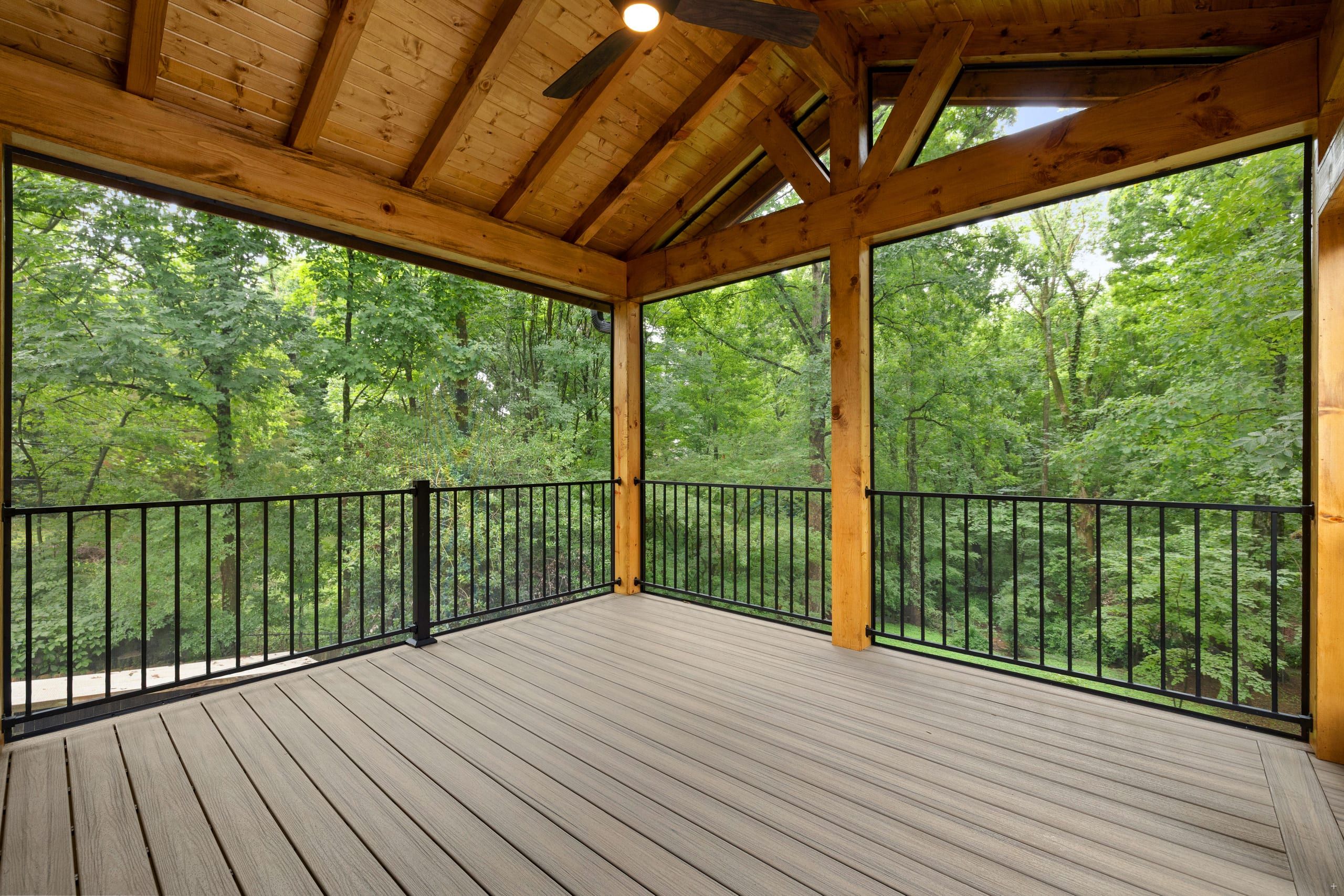 Corner of the Venice screened porch showing the vaulted cedar ceiling, ceiling fan, and black aluminum railing framing the tree line